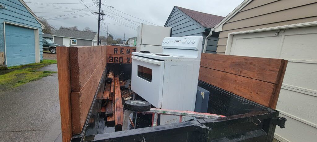 A truck bed loaded with appliances, including a white oven and refrigerator, parked outside.