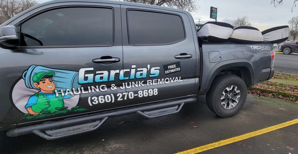Gray truck with mattresses, Garcia's Hauling & Junk Removal logo on the side, parked outside.