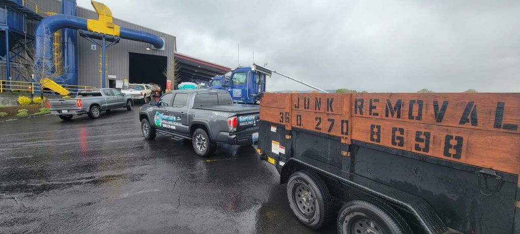 A truck pulling a trailer labeled Junk Removal. The scene is set in a rainy industrial area.