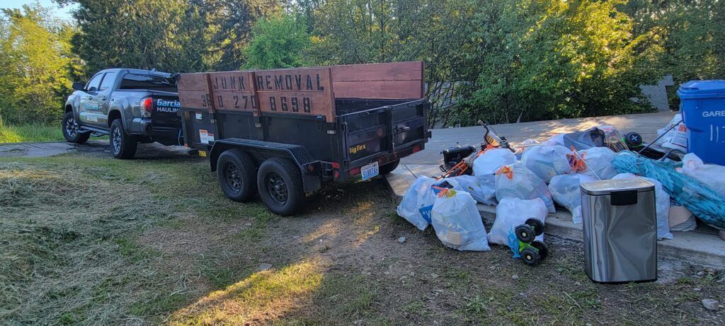 A truck towing a trailer next to bags of trash in a grassy area.
