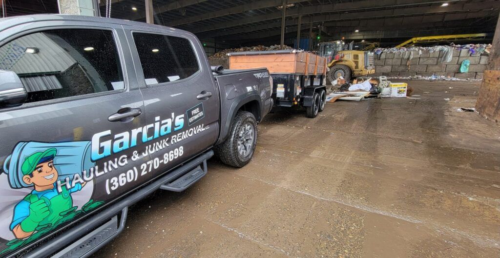 Grey pickup truck with trailer at a recycling center, Garcia's Hauling logo on the truck.