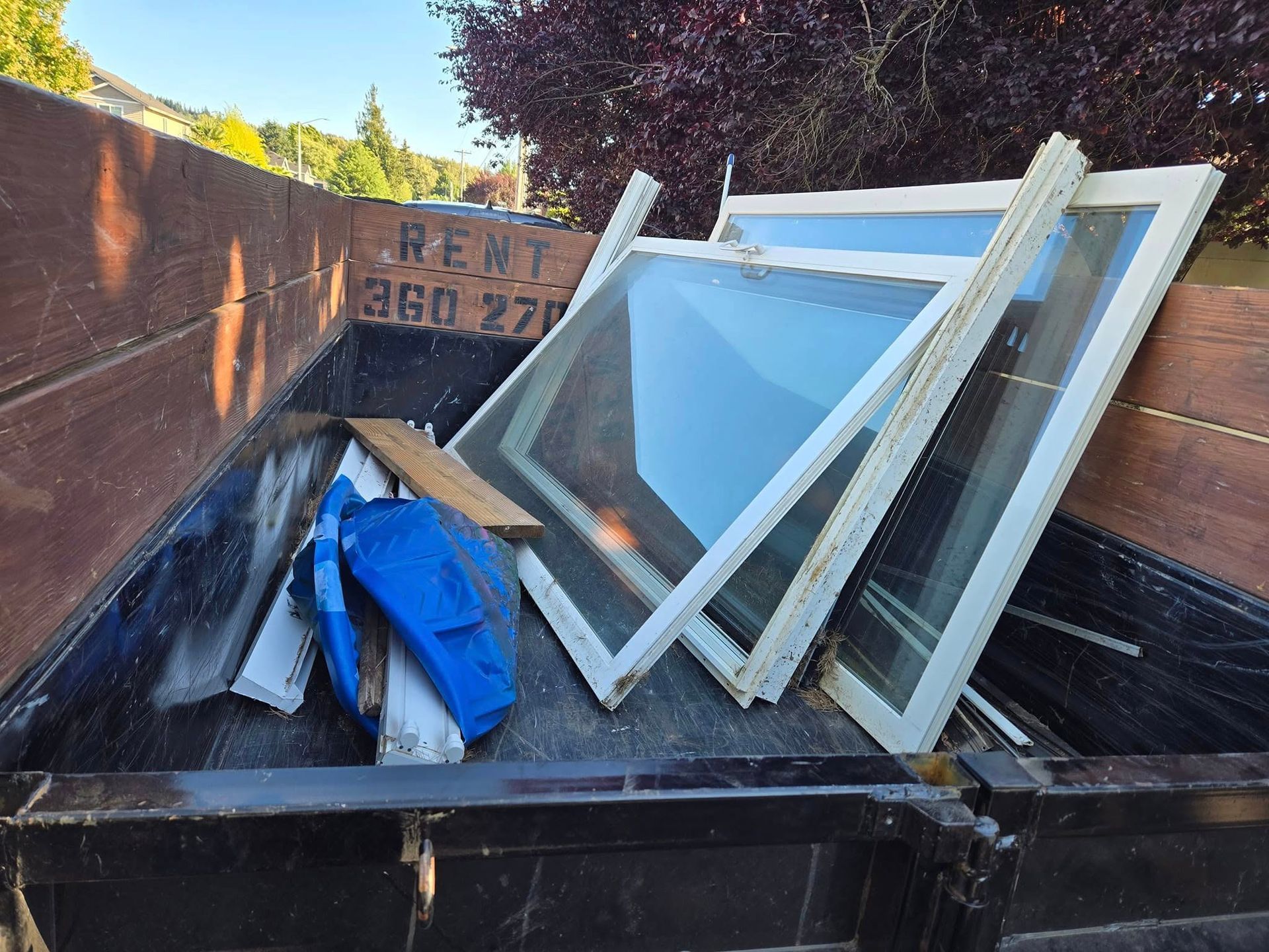 Dumpster filled with old white window frames and debris.