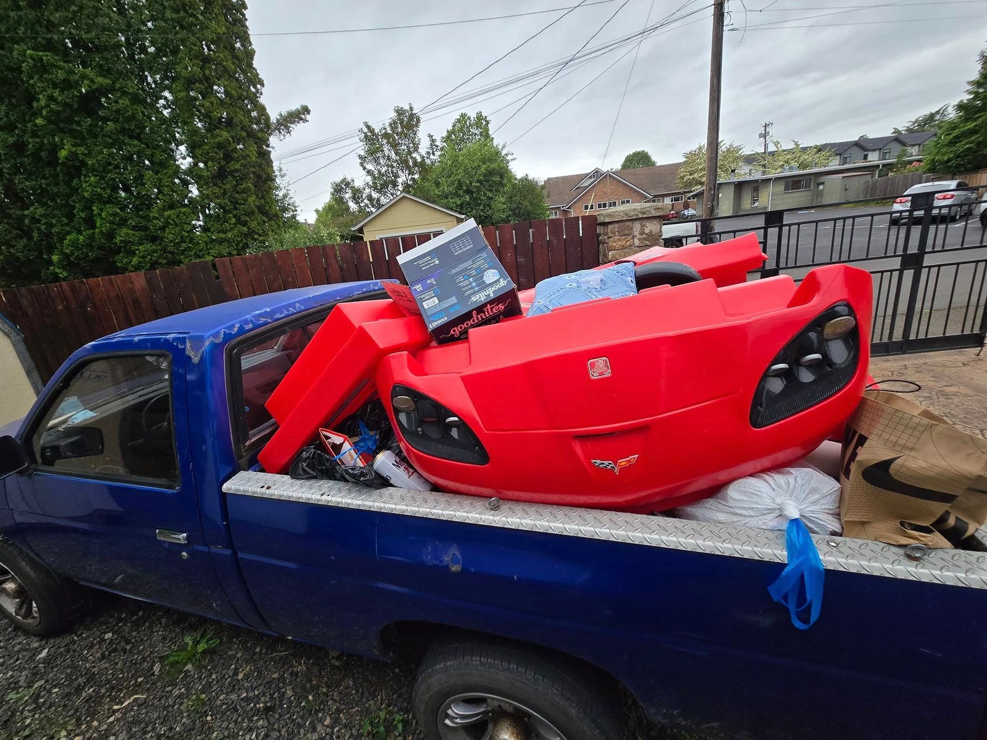 Blue pickup truck hauling red car body parts and an appliance.