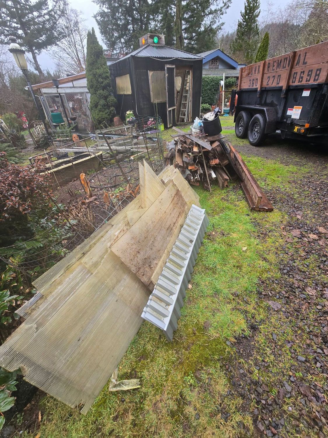 Debris pile with a shed, firewood, and a truck in a yard. Overcast day.