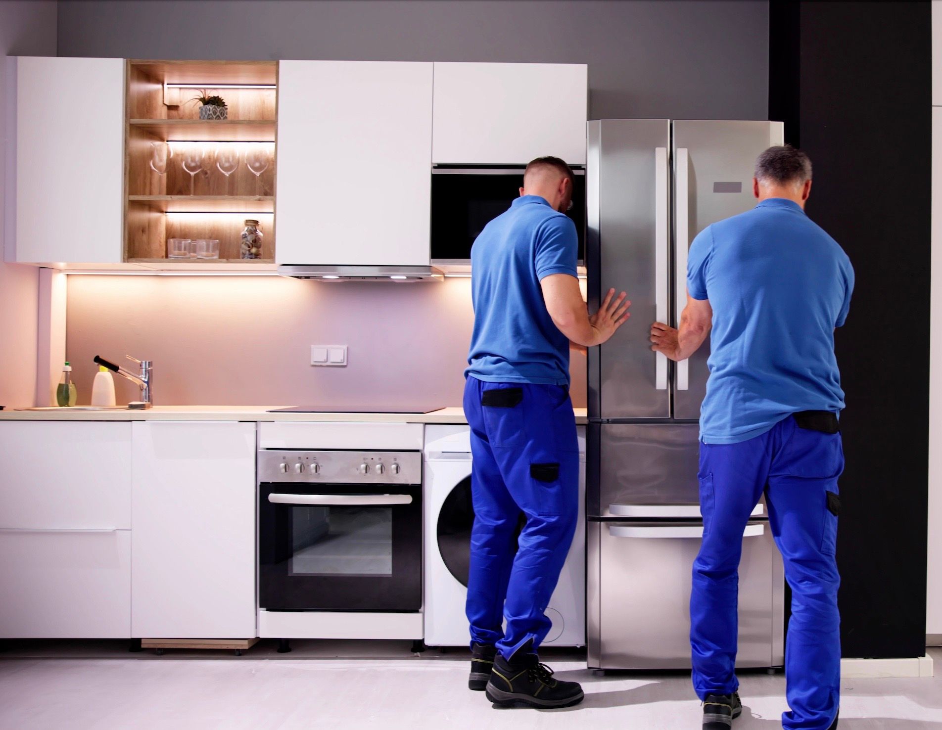 Two men are working on a refrigerator in a kitchen.