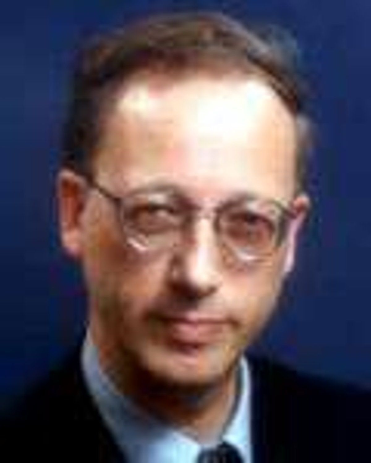 Man with glasses, wearing a suit, looking towards the viewer.