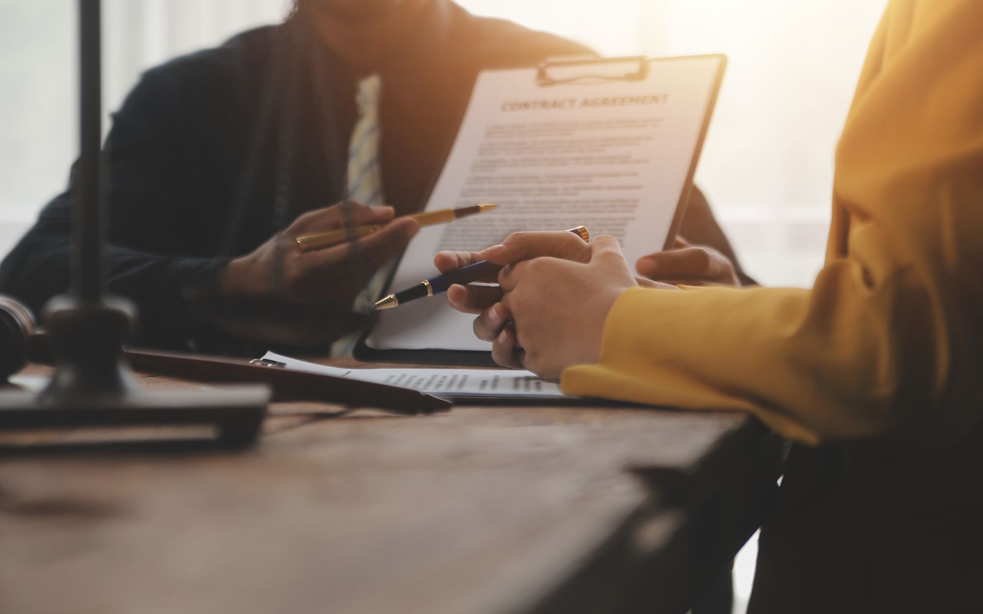 A person signing a contract with a pen, being guided by another person; indoors, office setting.