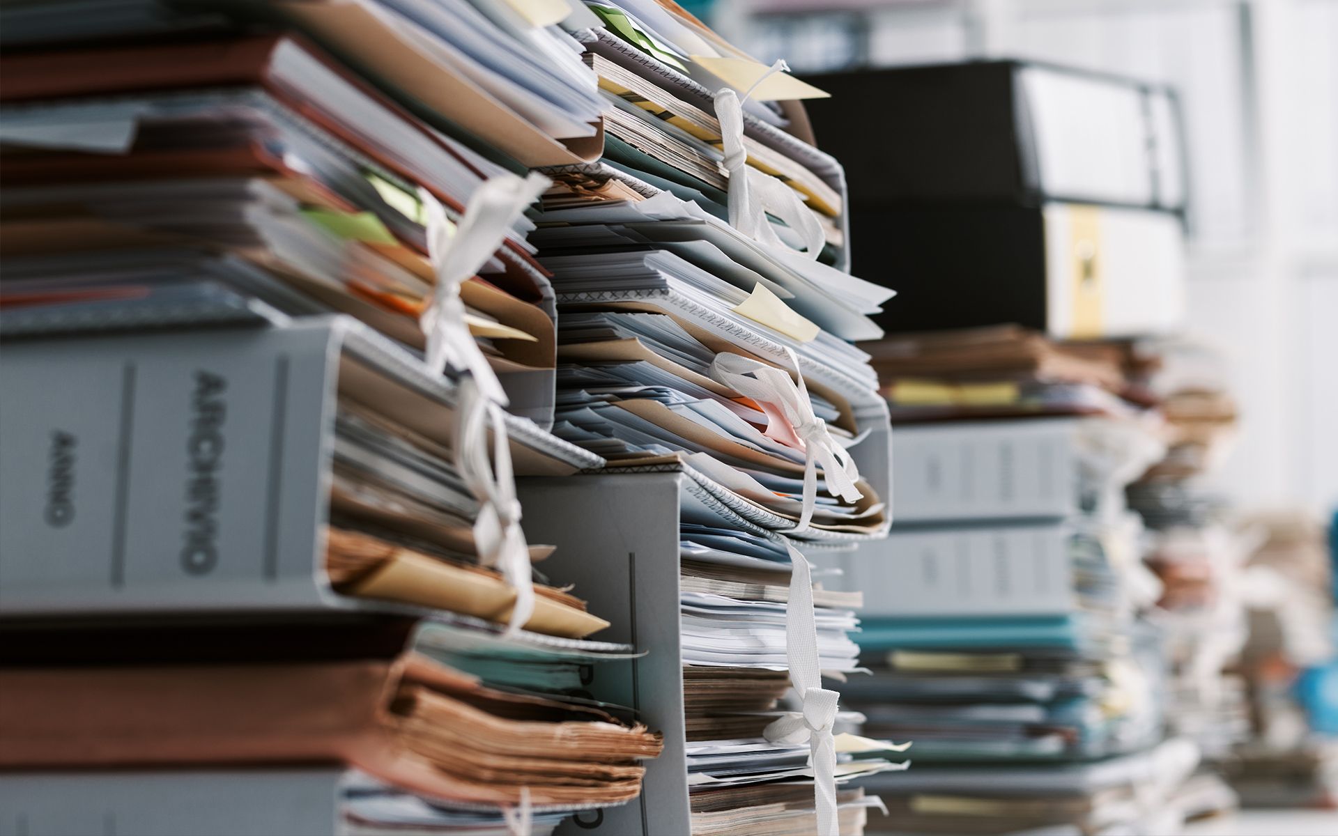 Stacks of papers and files, tied with string, overflowing a shelf in an office.