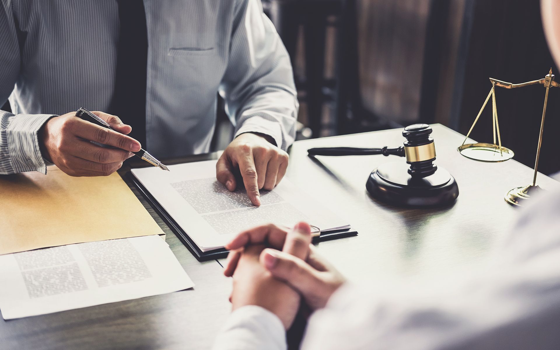 Two people in a law office reviewing paperwork with a gavel and scales of justice on the table.