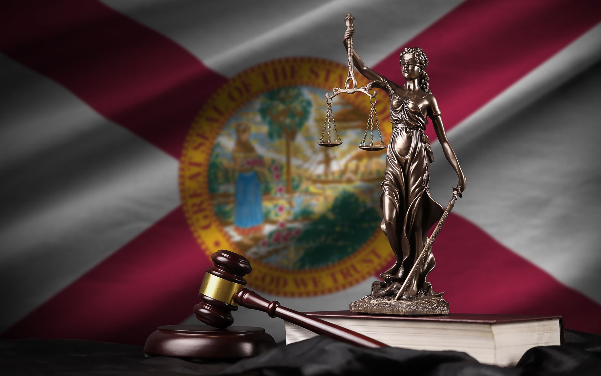Gavel and Lady Justice statue on law books, in front of the Florida state flag.