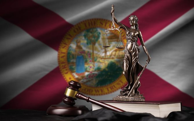 Gavel and Lady Justice statue on law books, in front of the Florida state flag.