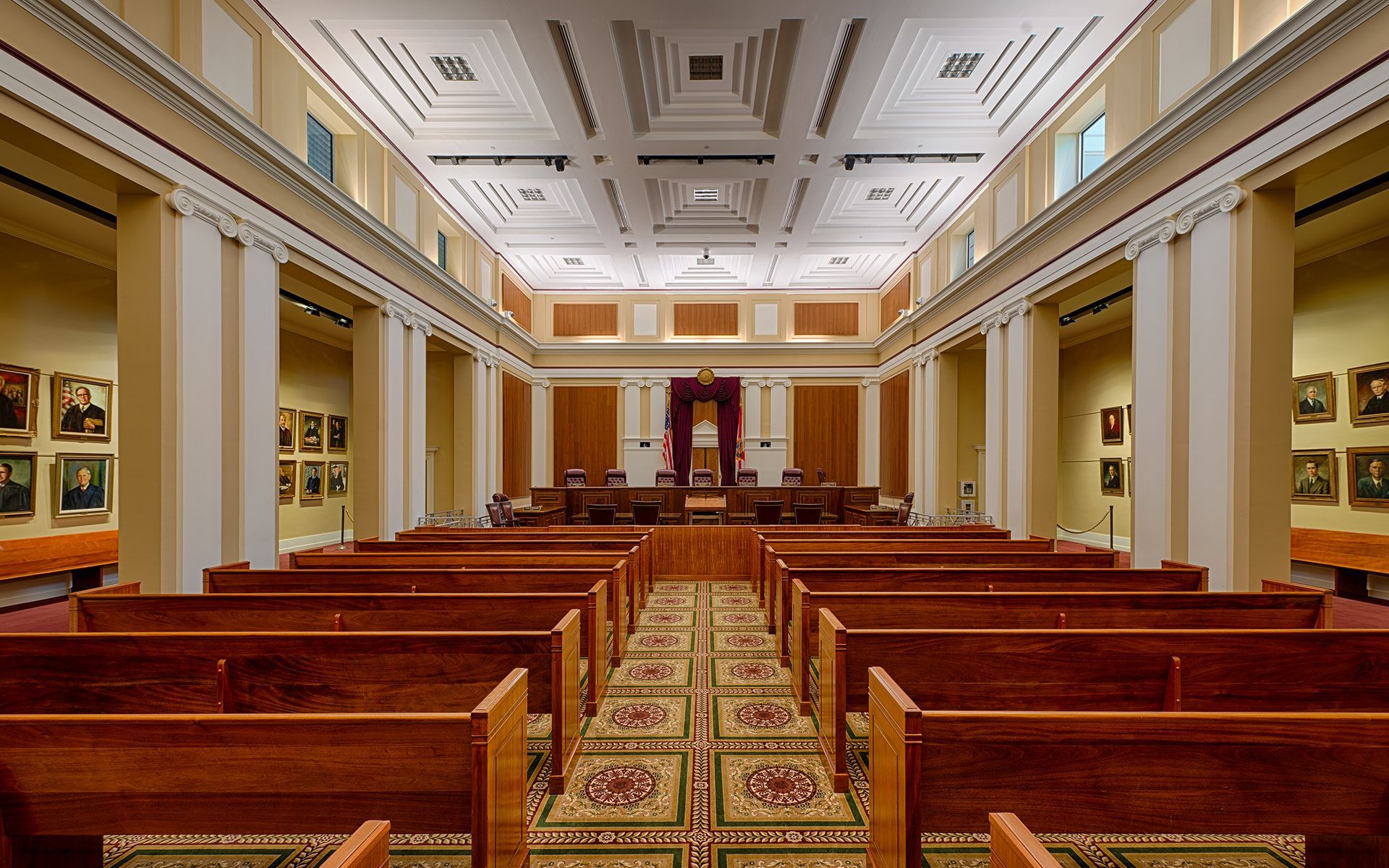 A large, wood-paneled courtroom with rows of pews, portraits, and pillars.