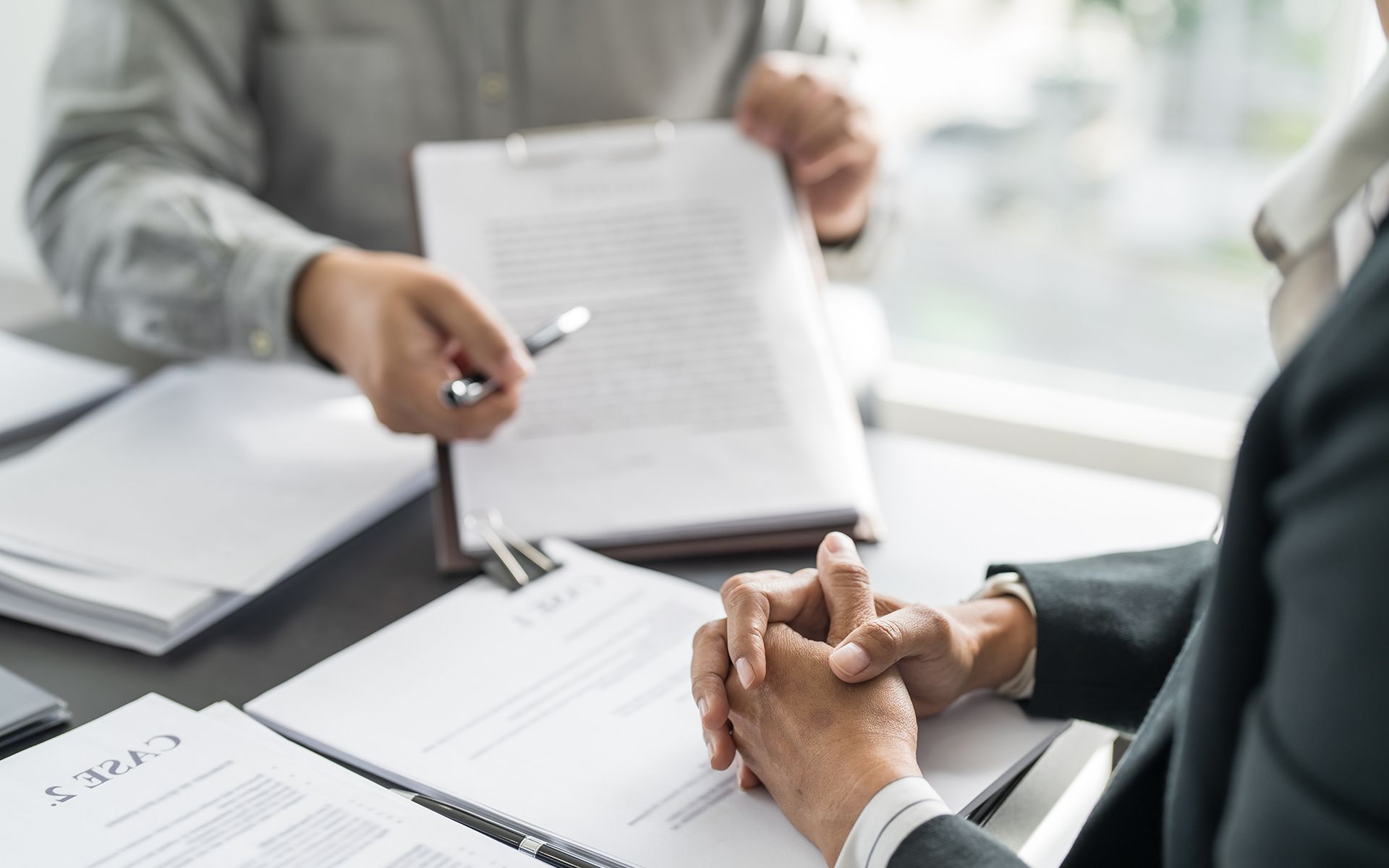 Two people at a desk reviewing paperwork. One points to a document, the other's hands clasped.