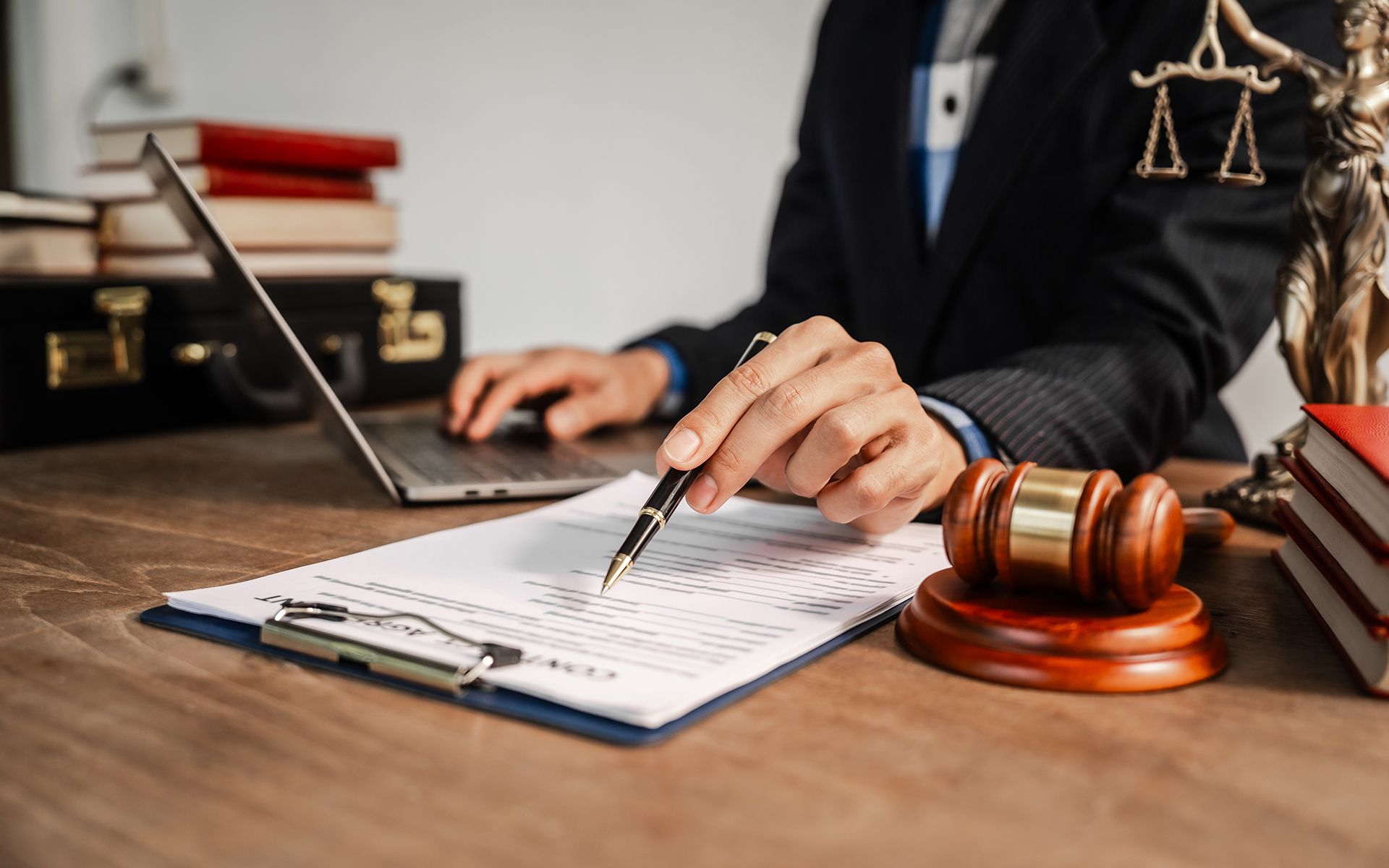 Lawyer reviewing paperwork, pointing with pen, next to a gavel, laptop, and books.