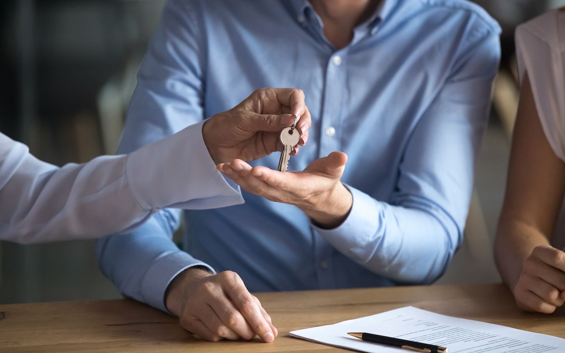 Person handing keys to another person, likely a real estate transaction, seated at a desk.
