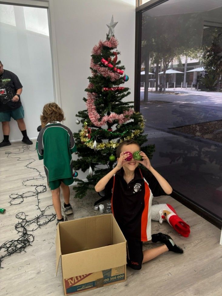 A Boy is Kneeling in Front of a Christmas Tree With a Box — Specialist Support Solutions in Rockhampton City, QLD