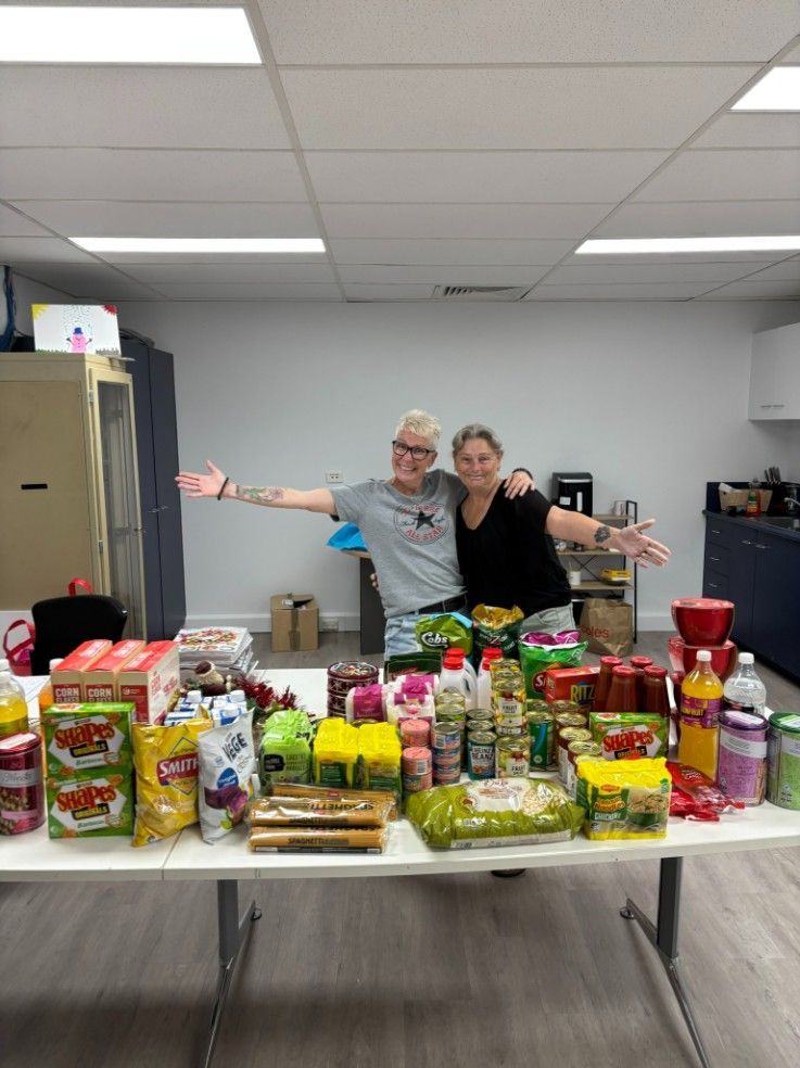Two Women Are Posing for a Picture in Front of a Table Full of Food — Specialist Support Solutions in Gladstone, QLD