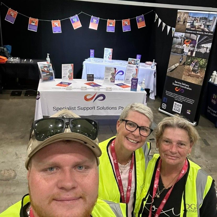 Three People Are Posing for a Picture in Front of a Table — Specialist Support Solutions in Rockhampton City, QLD