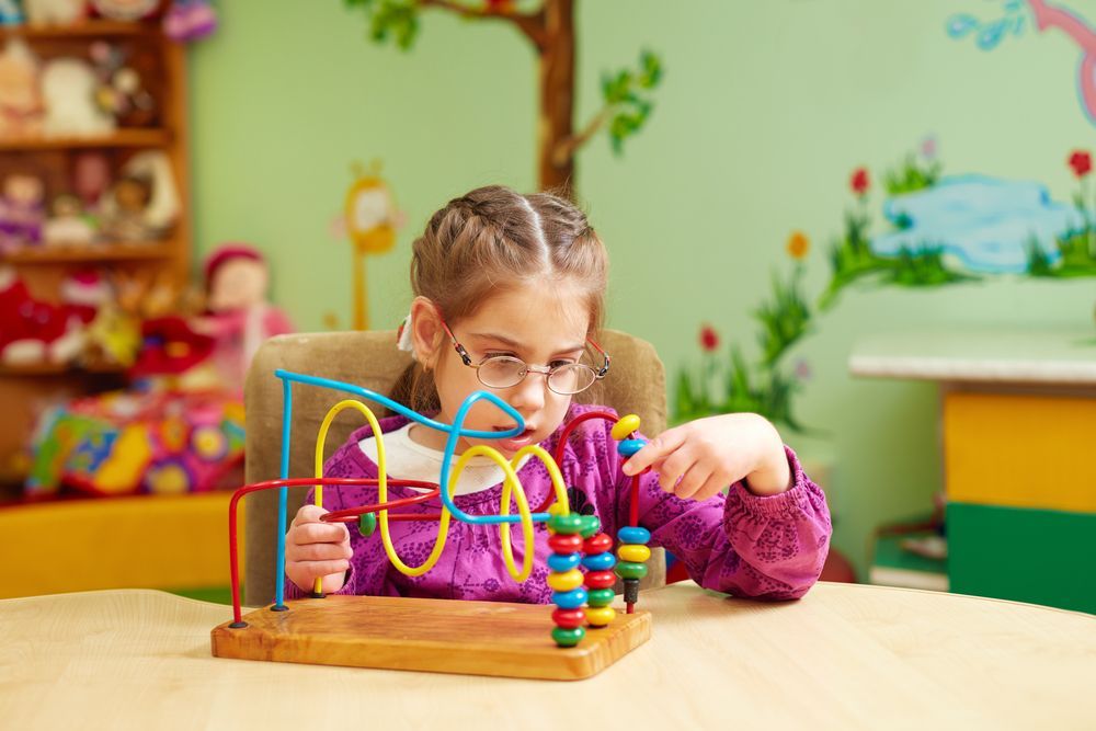 A Little Girl With Glasses is Playing With a Wooden Toy — Specialist Support Solutions in Emerald, QLD