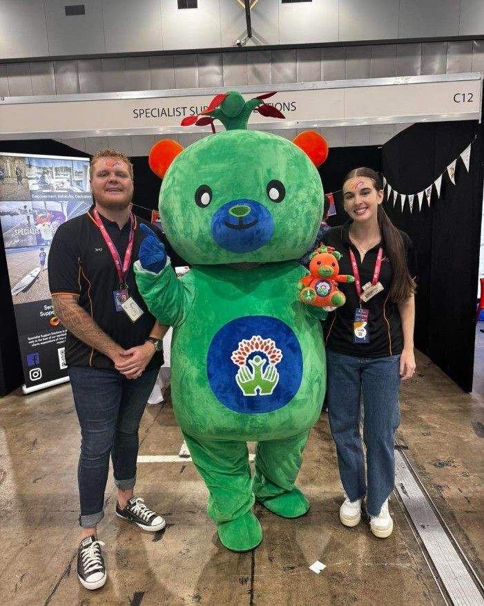 A Man and a Woman Are Standing Next to a Green Teddy Bear — Specialist Support Solutions in Rockhampton City, QLD