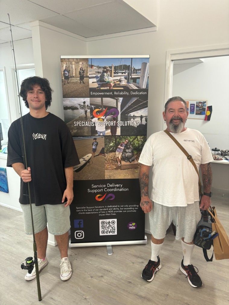 Two Men Are Standing Next to Each Other in Front of a Sign — Specialist Support Solutions in Rockhampton City, QLD