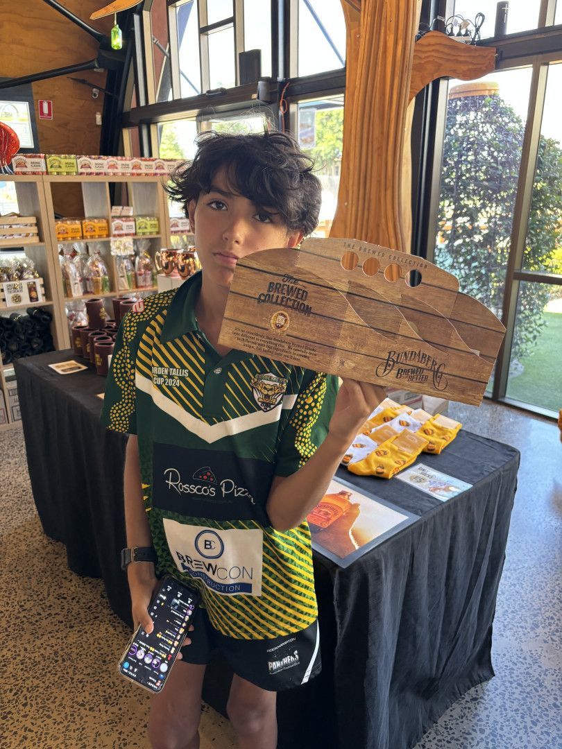 A person in a green and yellow sports shirt holds a signed wooden board in a retail space with display tables — Specialist Support Solutions in Rockhampton City, QLD