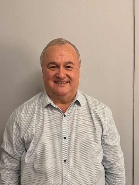 Man in a light blue patterned shirt smiling, standing against a gray wall — Bosco Accounting Pty Ltd In Warrawong, NSW
