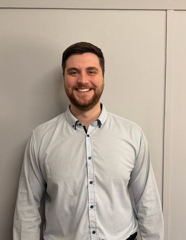 Man with beard smiles at the camera, wearing a button-down shirt, standing in front of a neutral-colored wall — Bosco Accounting Pty Ltd In Warrawong, NSW