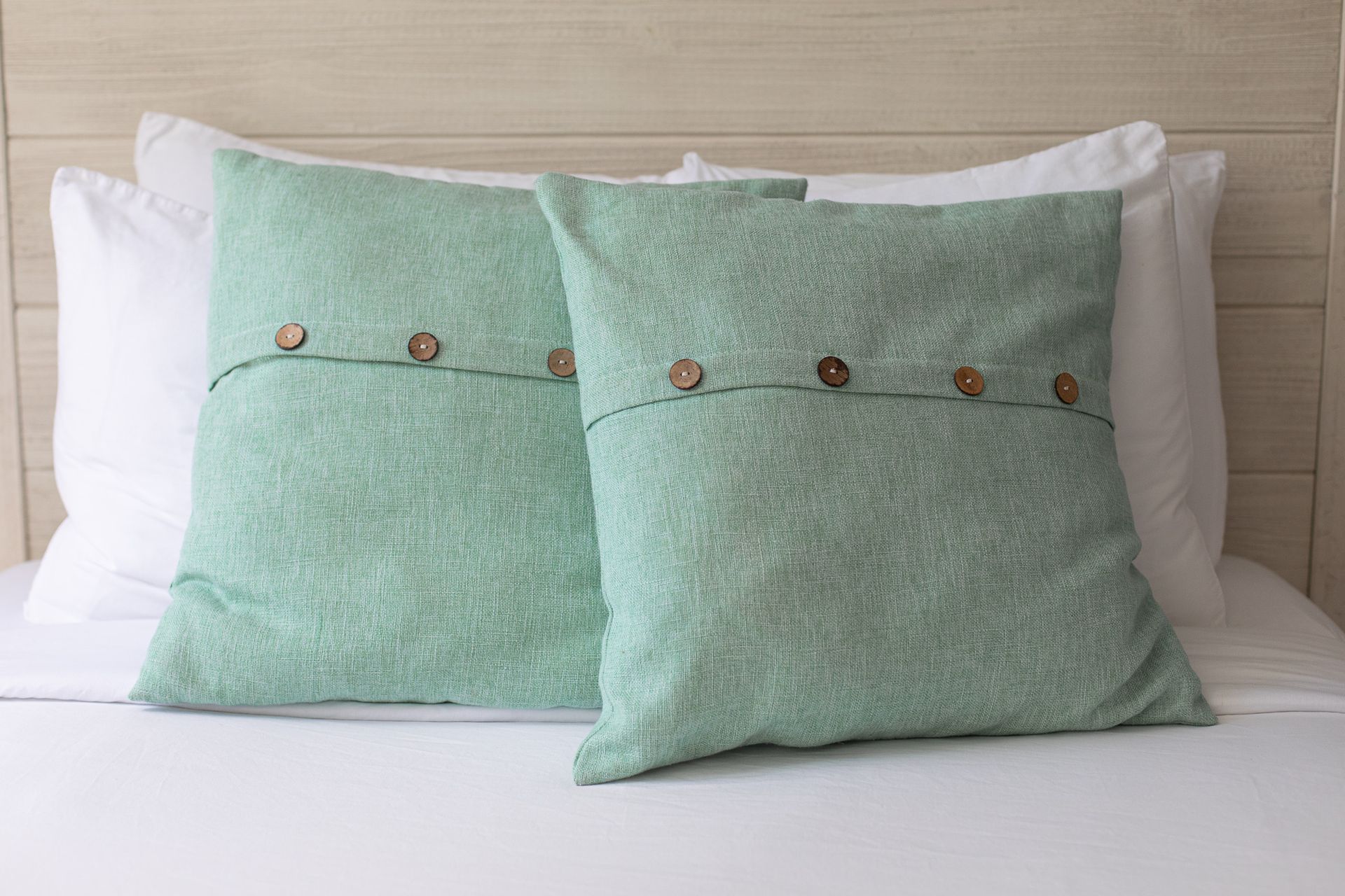 Two light green pillows with wooden buttons on a white bed.