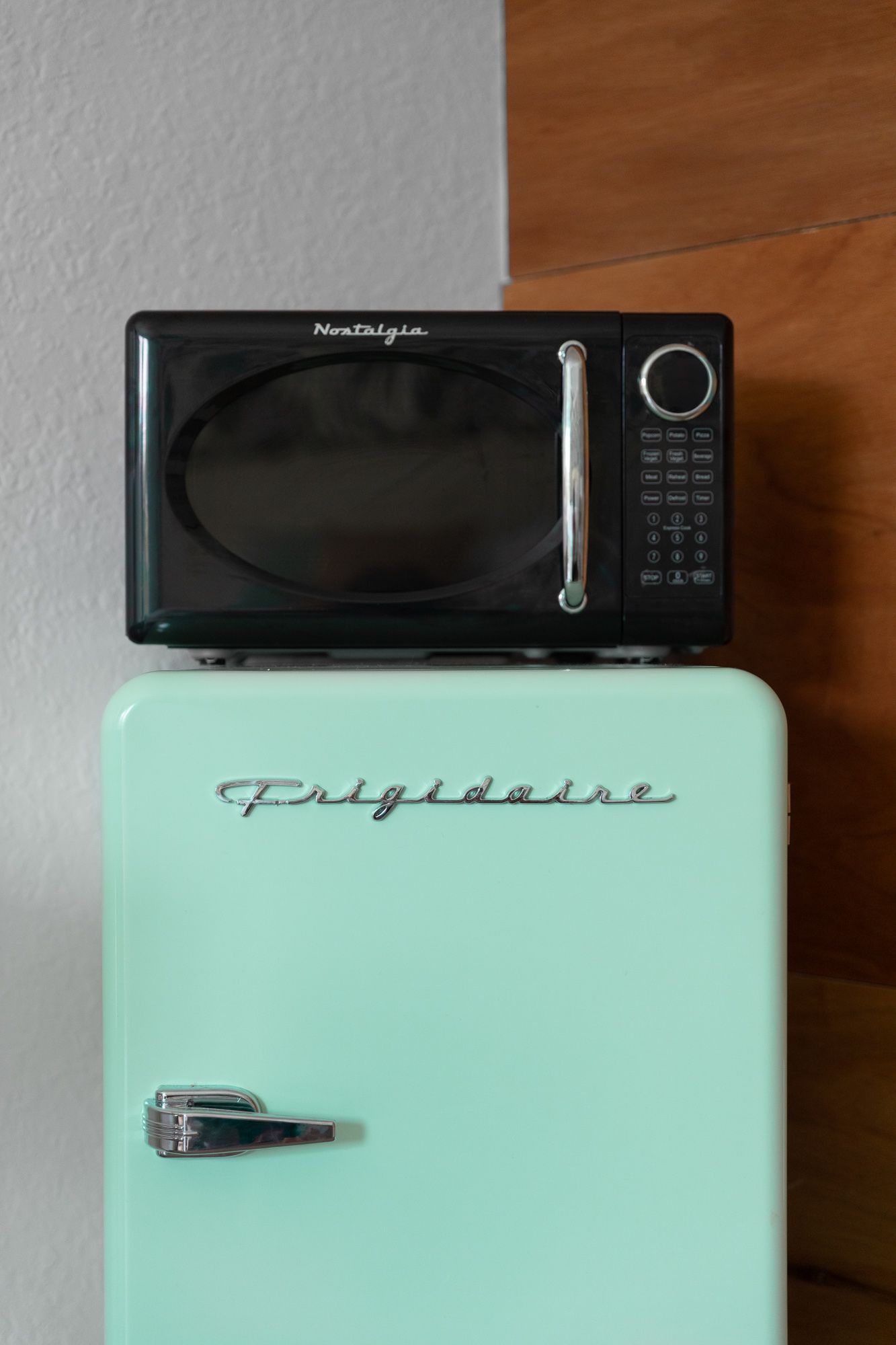 Black microwave atop a retro mint-green Frigidaire mini fridge.