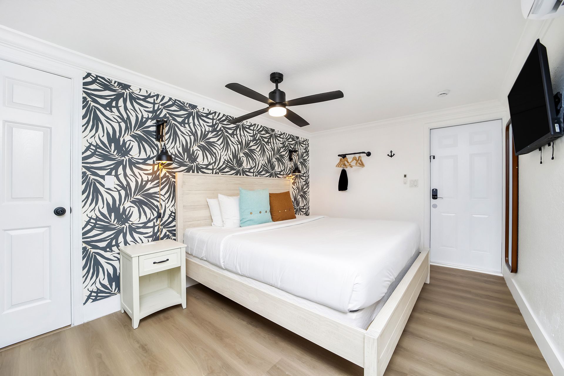 Bedroom with a white bed, patterned wallpaper, a TV, and white doors.