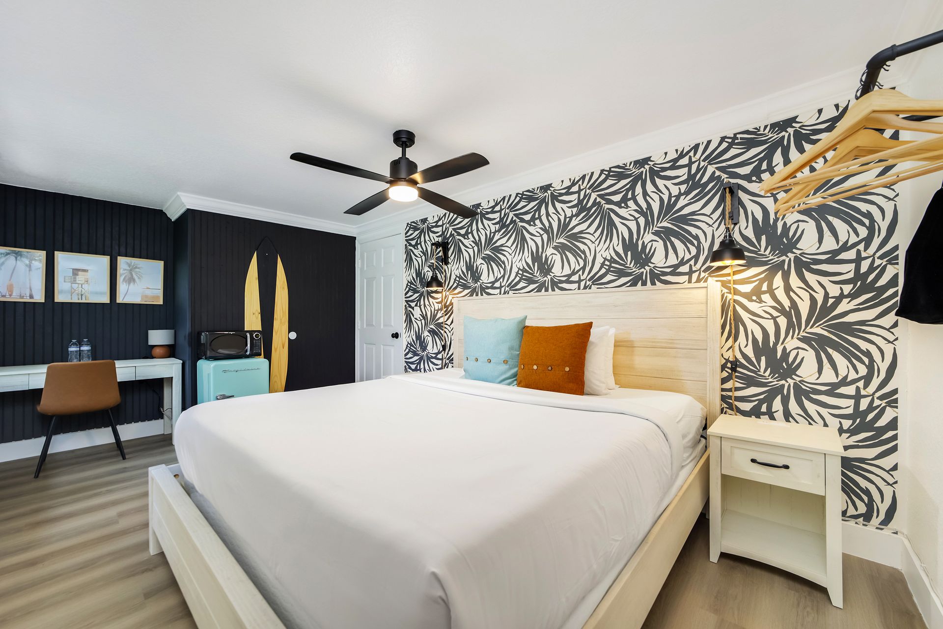 Bedroom with king bed, tropical wallpaper, desk, surfboard. Modern design, bright.