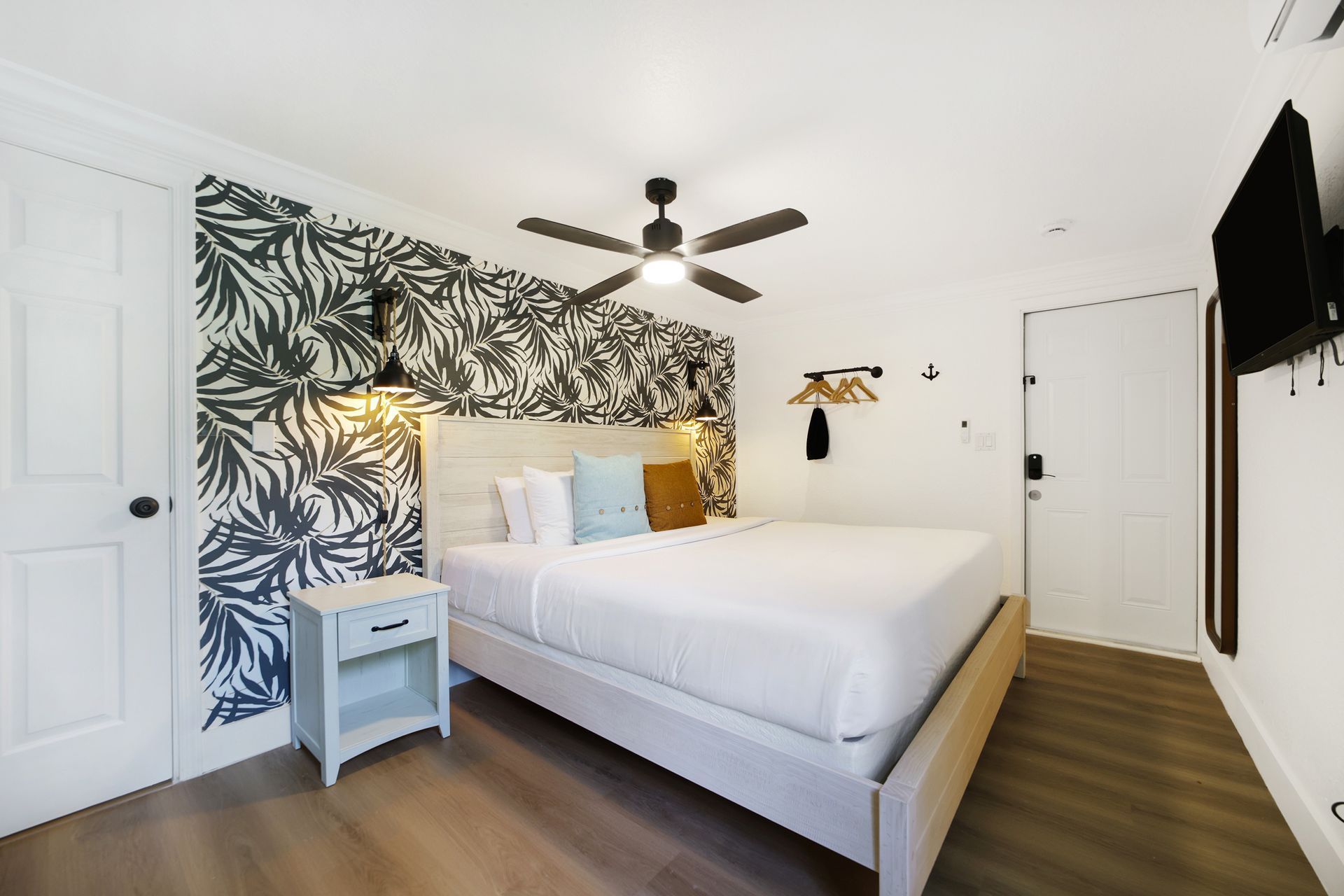 Bedroom with a queen bed, wallpaper accent wall, nightstand, and television.