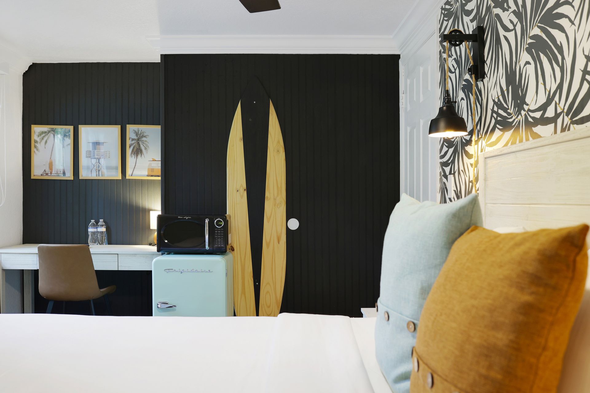 Bedroom with white bed, desk, and black accent wall with wooden surfboard art.