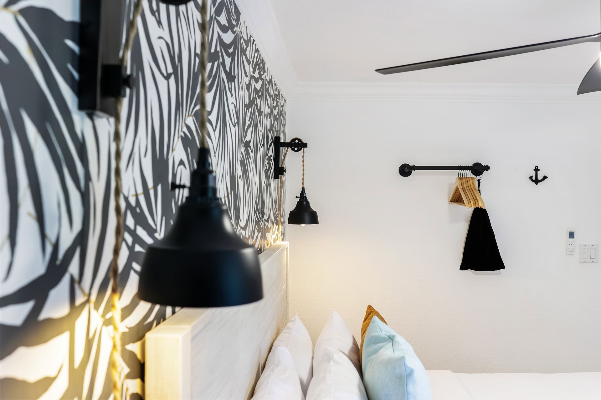 Bedroom corner: black pendant lamp, patterned accent wall, white bedding, nautical decor.