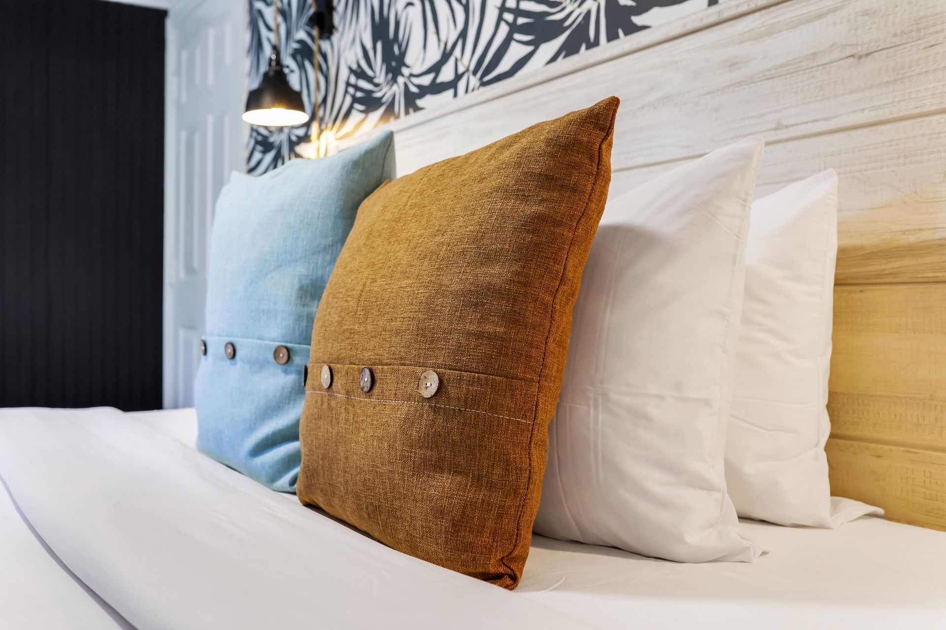 Pillows in varying colors on a bed in a room with tropical-themed wallpaper.