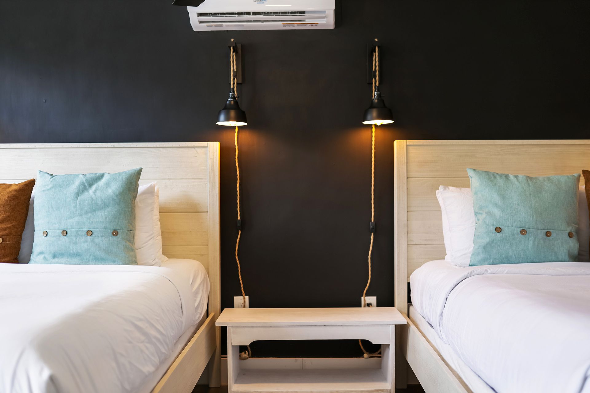 Two beds in a room with a dark accent wall, bedside table, and sconce lighting.