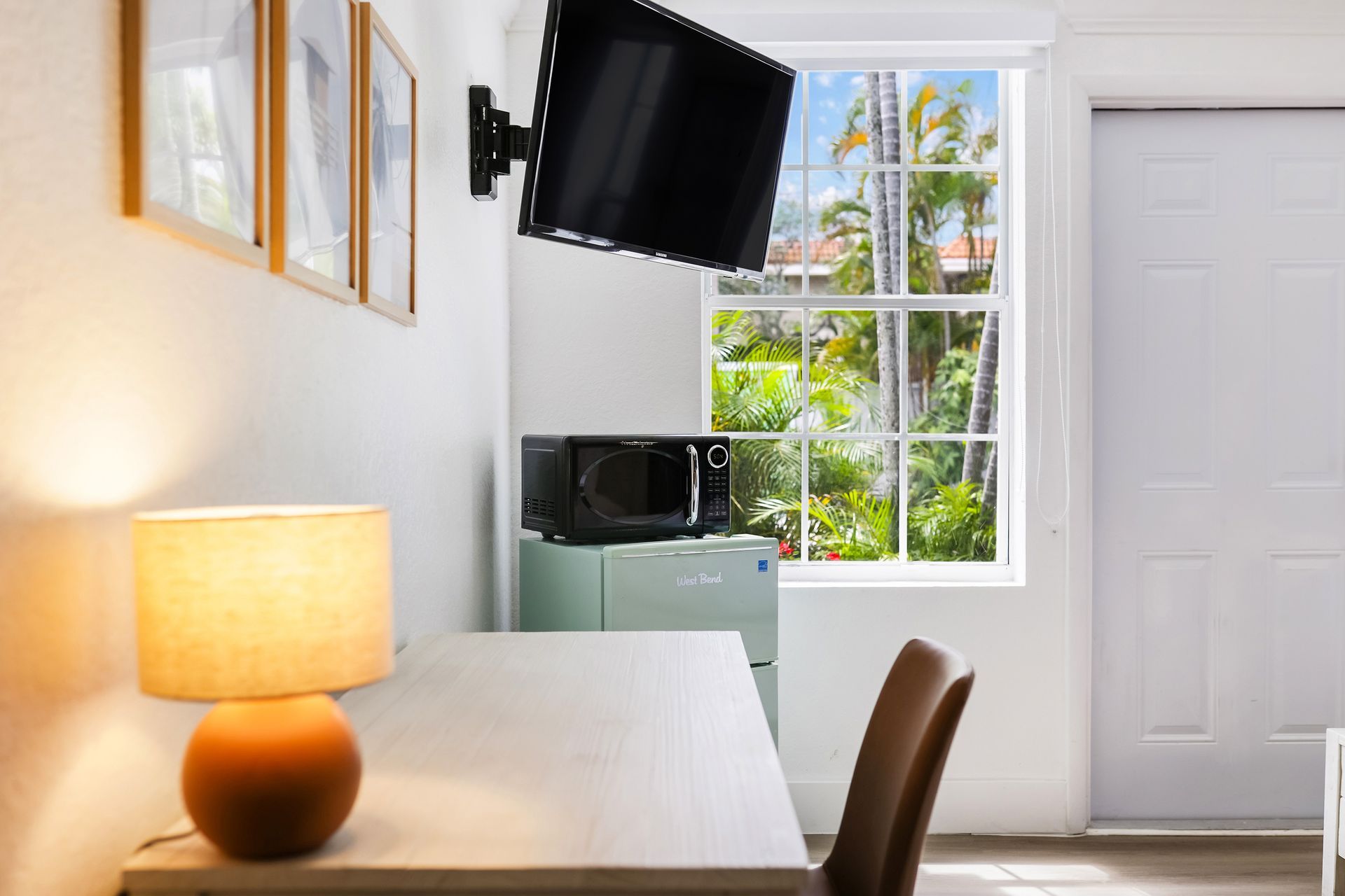 Small room with desk, lamp, TV, microwave, mini-fridge, and window.