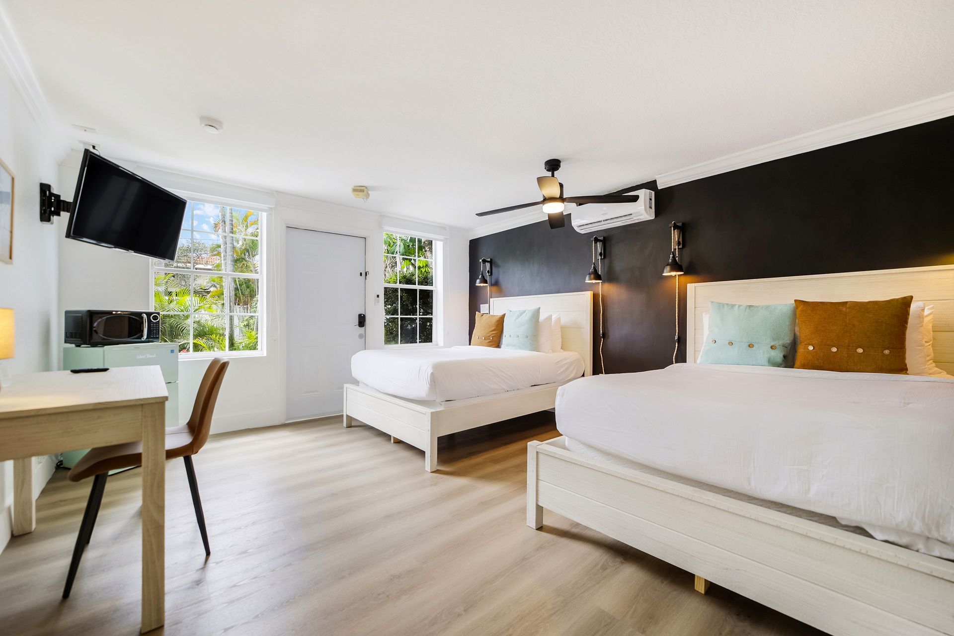 Hotel room with two white beds, a desk, and a TV. Sunlight streams through the window.