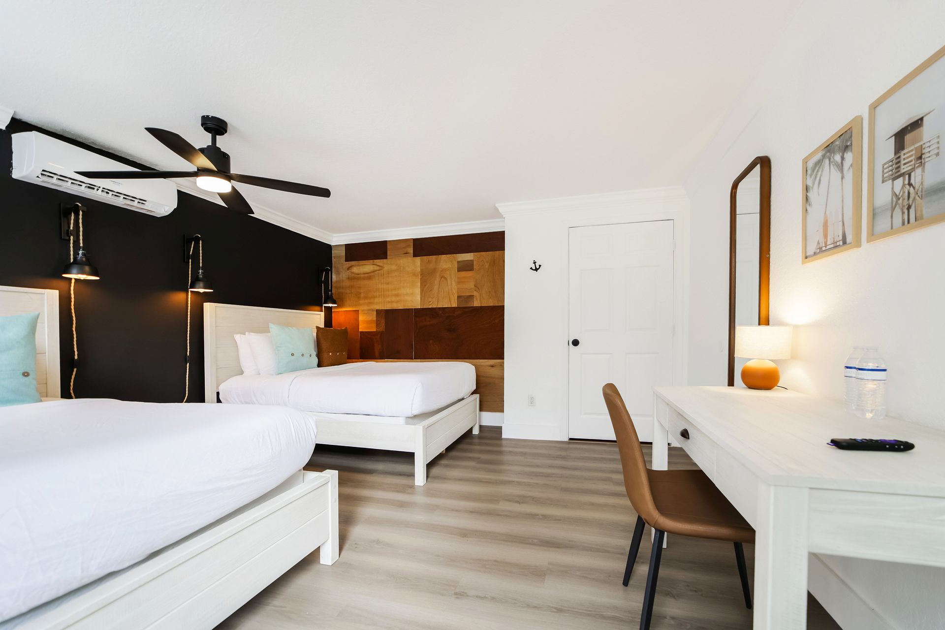 Hotel room with two beds, desk, and a wall with textured wood paneling and black accents.