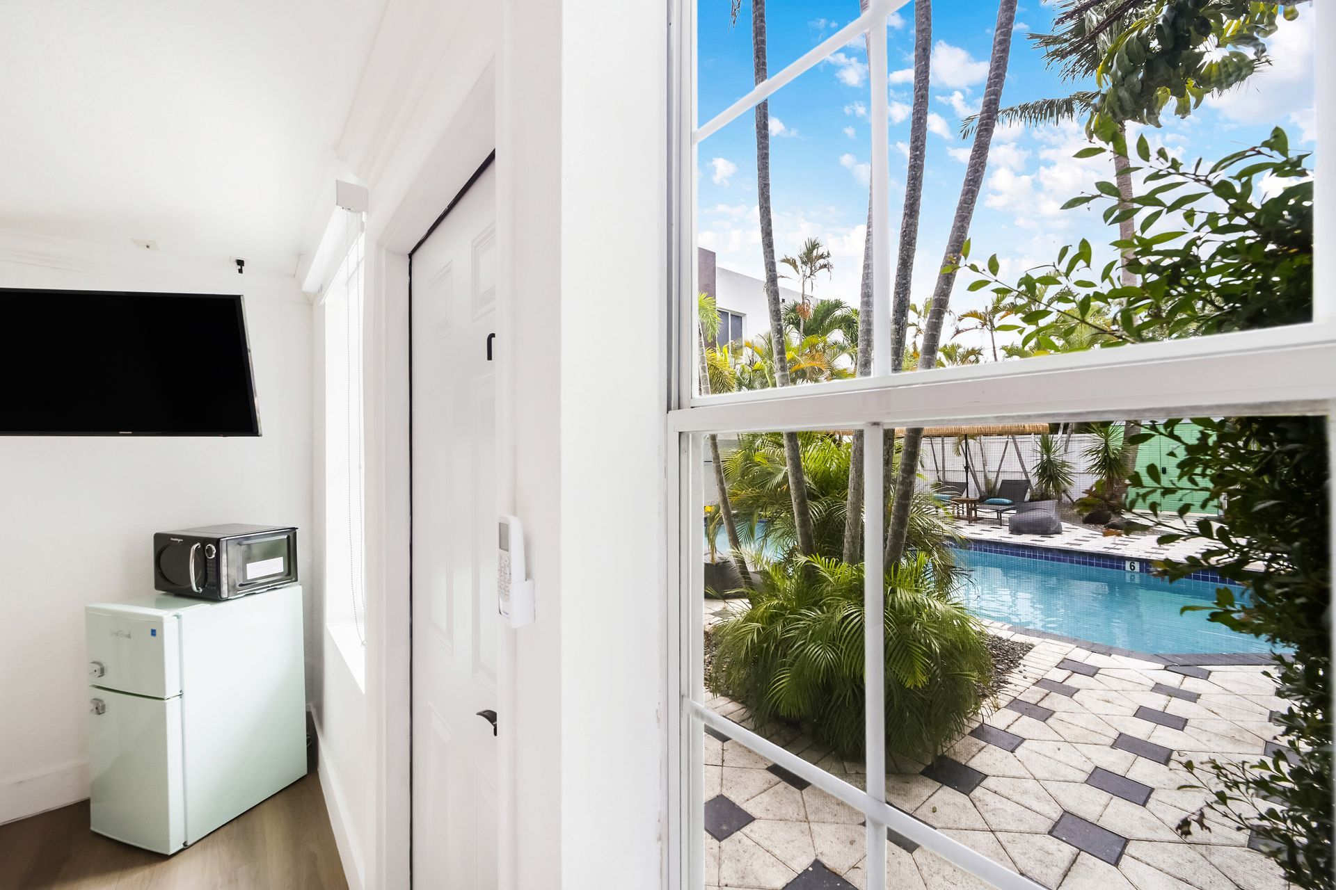 Interior view of a room with a window overlooking a pool. TV, retro refrigerator, and a door are also visible.