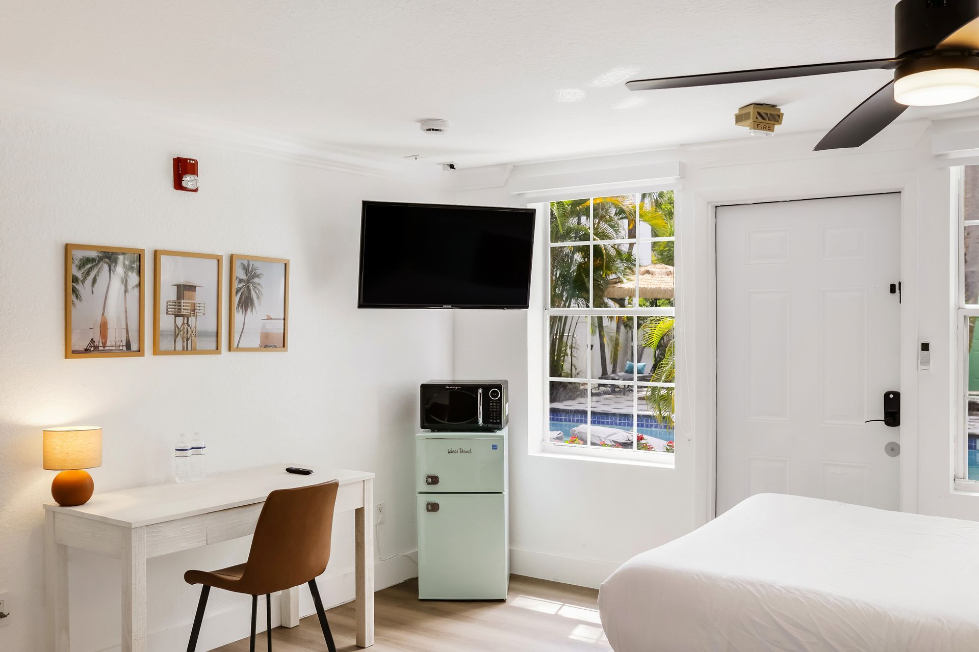 Hotel room with a desk, TV, refrigerator, window, and bed.