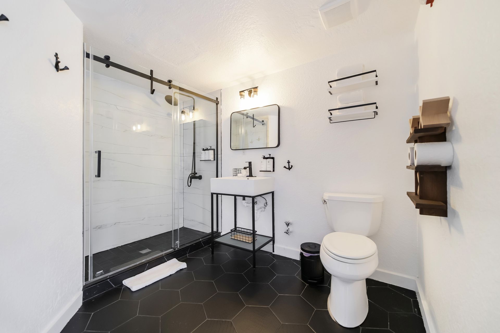 Bathroom with shower, vanity, toilet, and black hexagon tile floor. White walls.