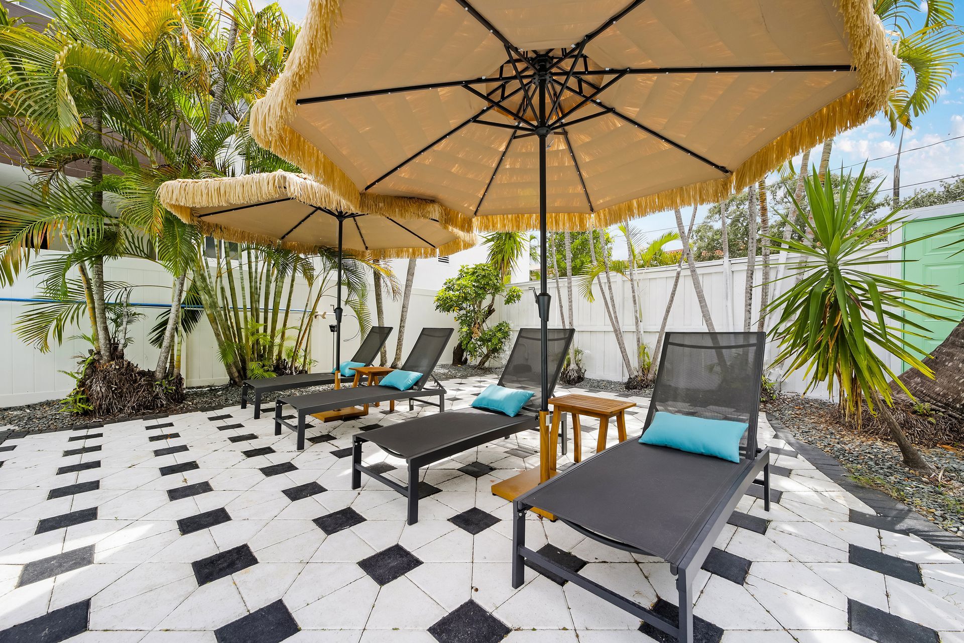 Patio with black and white tiled floor, lounge chairs, fringed umbrellas.