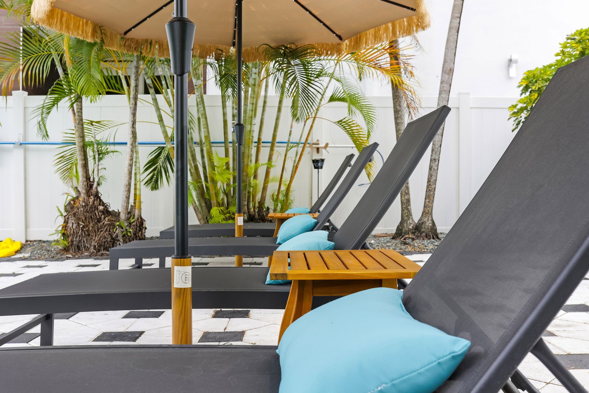 Poolside lounge chairs with turquoise pillows, under a yellow umbrella.