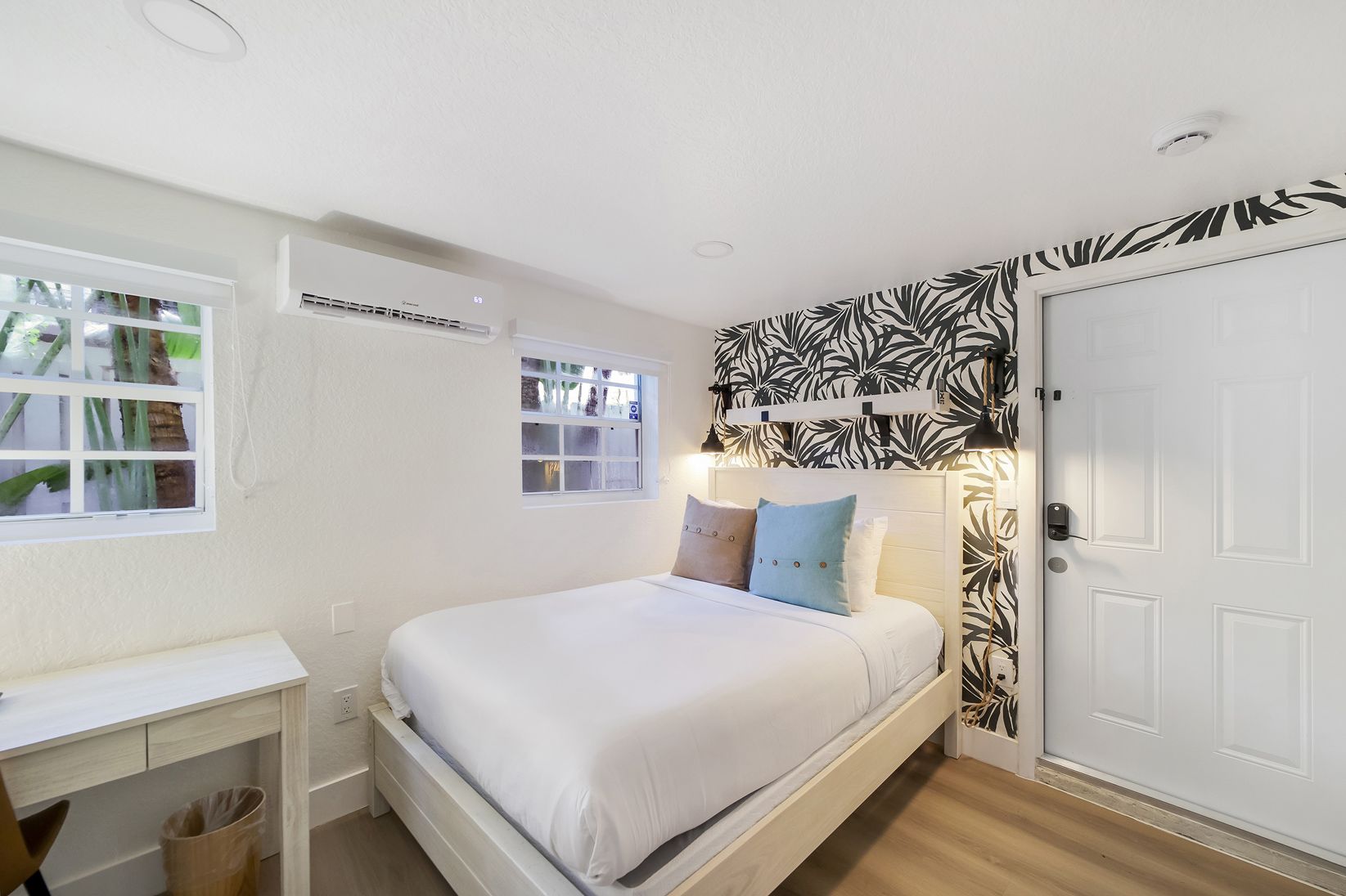 Small bedroom with a bed, desk, and door; white walls, black patterned accent wall, two windows.