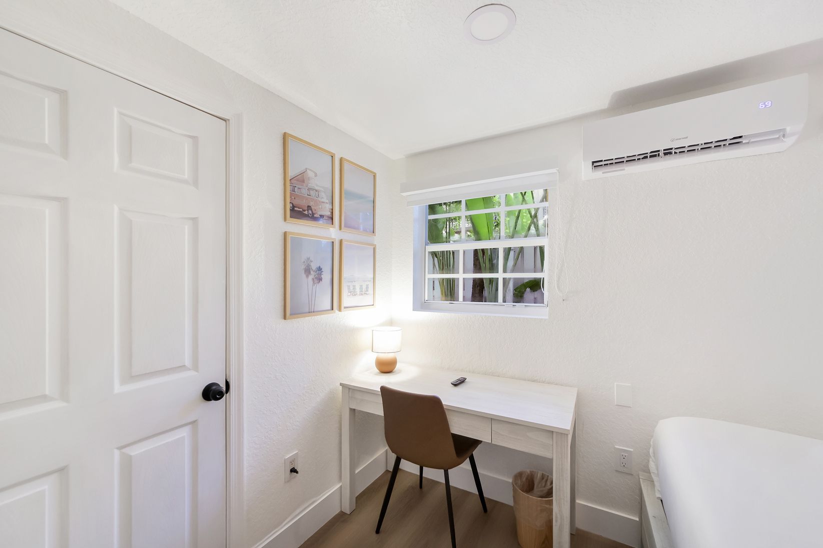 Small white room with desk, chair, window, artwork, and air conditioner.