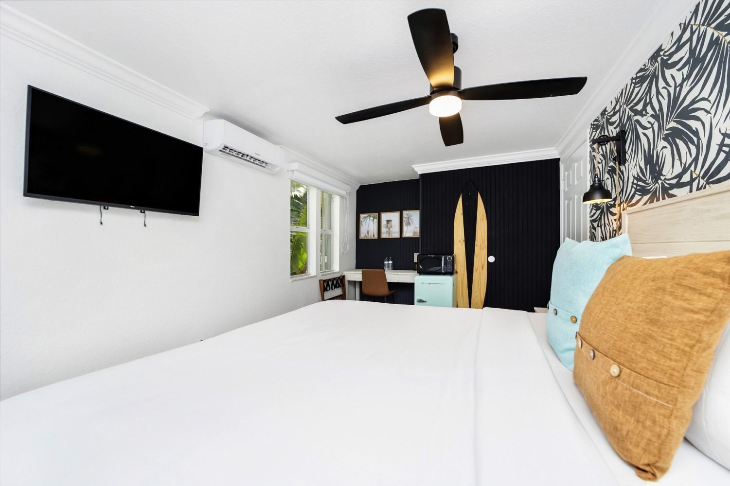 Bedroom with white walls, large bed, black TV, ceiling fan, and surfboard decor.