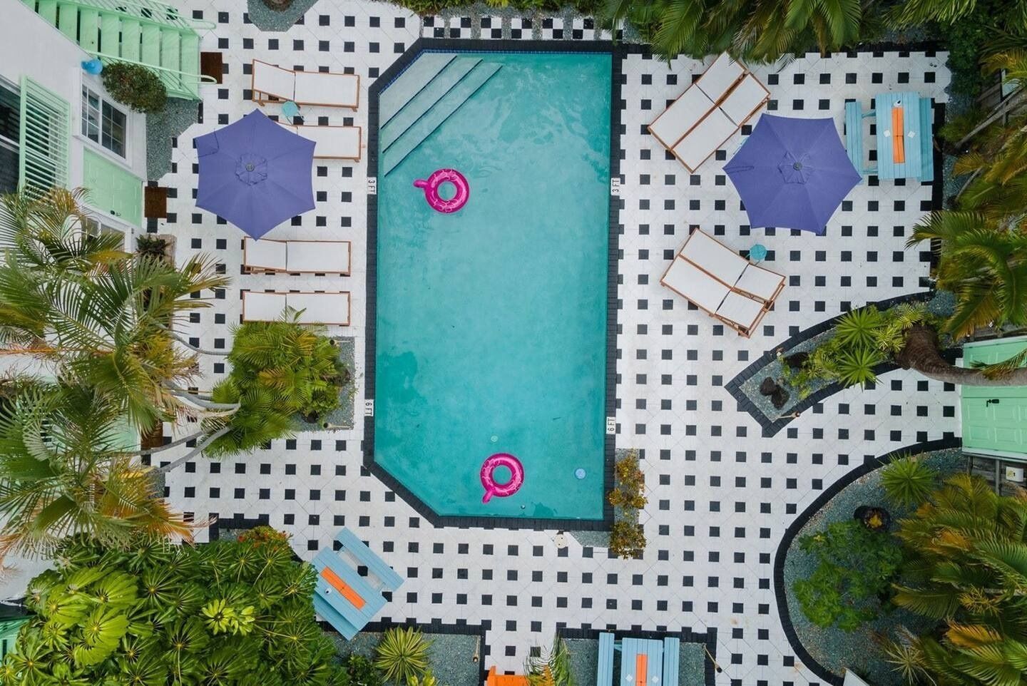 Aerial view of a rectangular pool with two pink floats surrounded by lounge chairs, umbrellas, and patterned pavement.