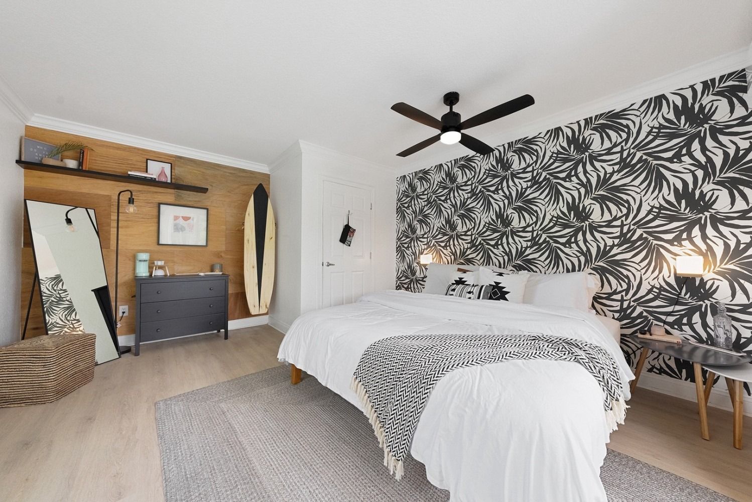Bedroom with floral wallpaper accent wall, surfboard, black dresser, and neutral rug.